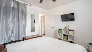 Ein Schlafzimmer mit einem großen Bett, einem Deckenventilator, einem an der Wand montierten Fernseher und einem Kleiderschrank mit Aufbewahrungsboxen.