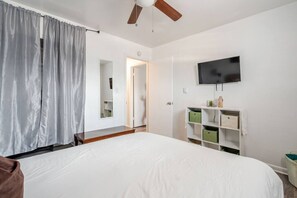 Ein Schlafzimmer mit einem großen Bett, einem Deckenventilator, einem an der Wand montierten Fernseher und einem Kleiderschrank mit Aufbewahrungsboxen.