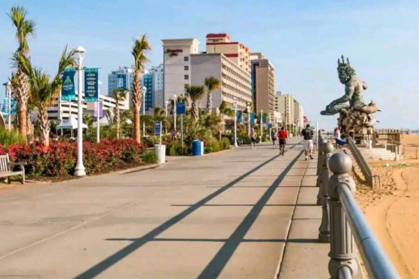 A coastal promenade with a statue, palm trees, and modern buildings in the background.