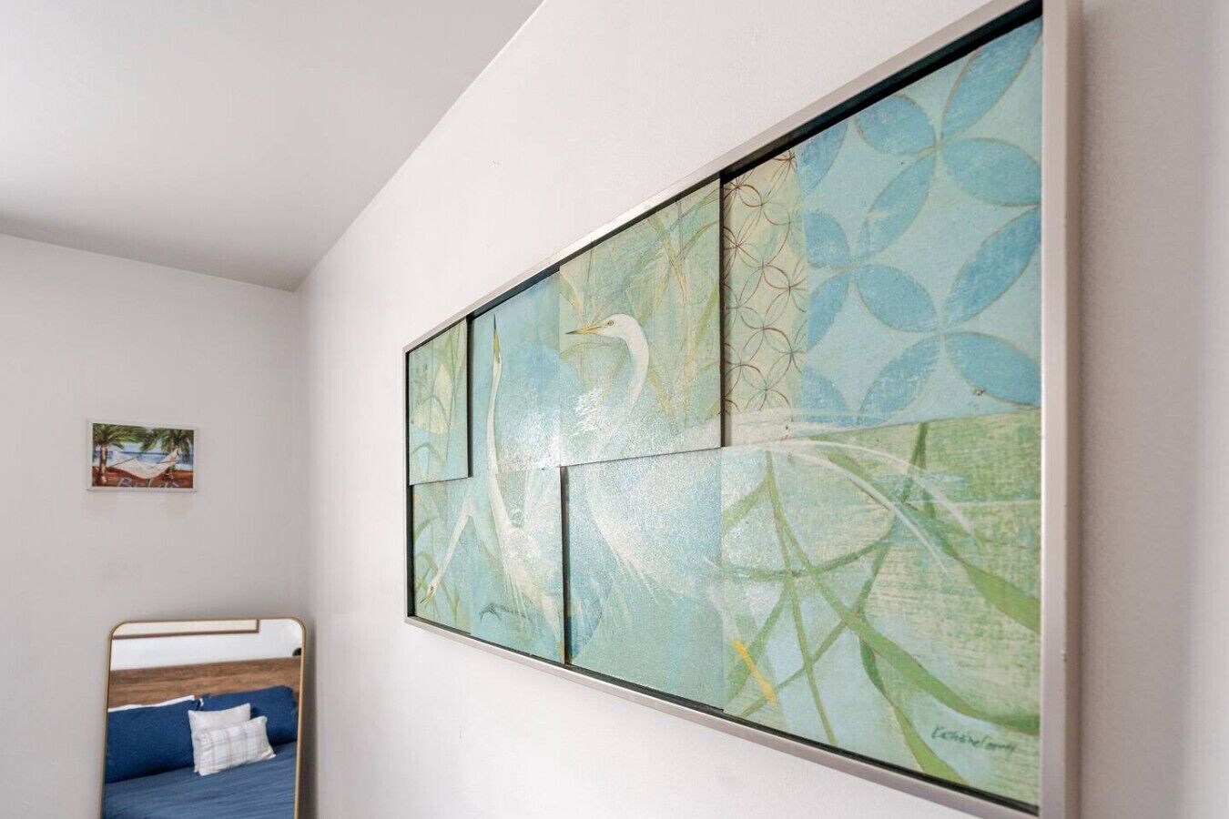 A bedroom with a bed, a wall-mounted artwork, and a small framed picture on the wall.