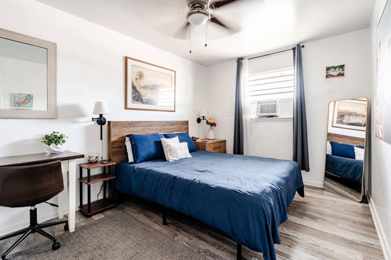 A bedroom with a bed, a desk, a chair, a ceiling fan, and a window with curtains.