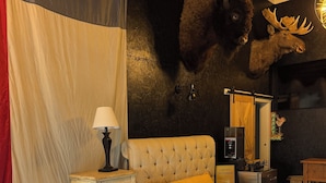 A bedroom with a tufted headboard, a bed with striped bedding, a bench, a lamp, and a wall-mounted mirror. - Hill Country Estate on 11 Acres near Dripping Springs and Wimberley (Wimberley)