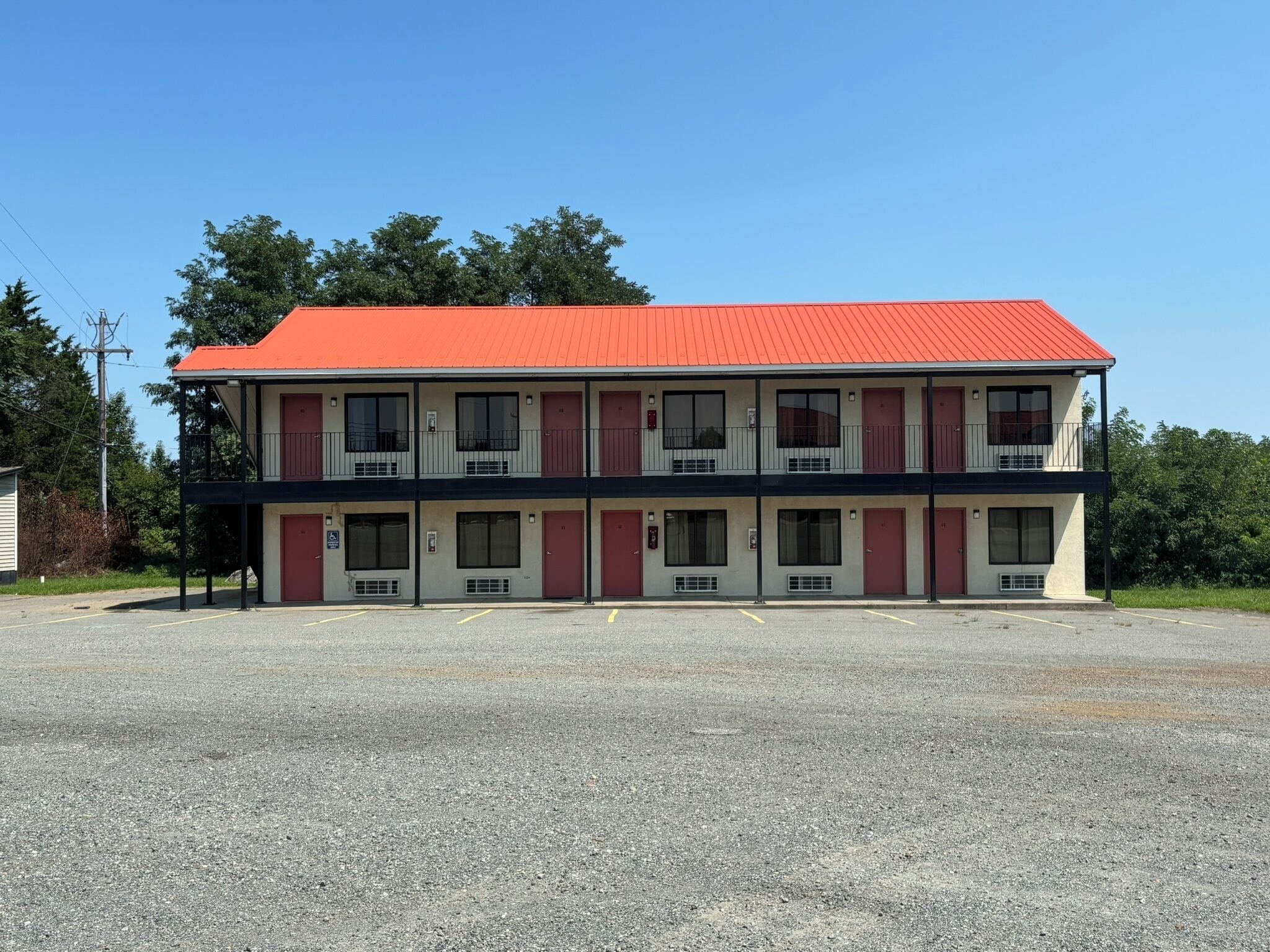 Un motel de dos pisos con techo rojo, varias ventanas y un estacionamiento al frente.