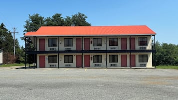 Un motel de dos pisos con techo rojo, varias ventanas y un estacionamiento al frente.