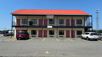 A motel with a red roof, multiple rooms, and a parking lot with several cars.