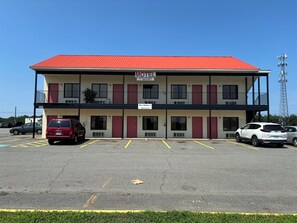 A motel with a red roof, multiple rooms, and a parking lot with several cars. - Trail Motel (Ruckersville)