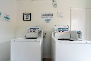 A laundry facility with two washing machines, a notice sign, and a wall-mounted sign indicating the services provided. - Ocean Breeze 2BR Apt by Wavepool (Virginia Beach)
