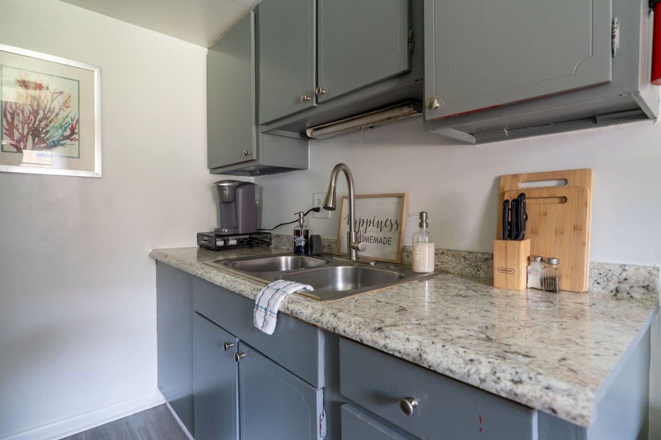 A kitchen with grey cabinets, a granite countertop, a coffee maker, a soap dispenser, and a wooden cutting board with knives.