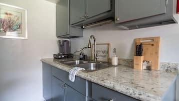 A kitchen with grey cabinets, a granite countertop, a coffee maker, a soap dispenser, and a wooden cutting board with knives.