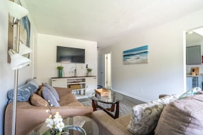 A living room with a sofa, armchairs, a coffee table, and a flat-screen TV mounted on the wall. - Ocean Breeze 2BR Apt by Wavepool (Virginia Beach)