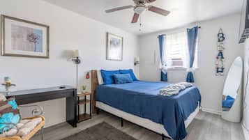 Een slaapkamer met een bed, bureau, stoel en plafondventilator.