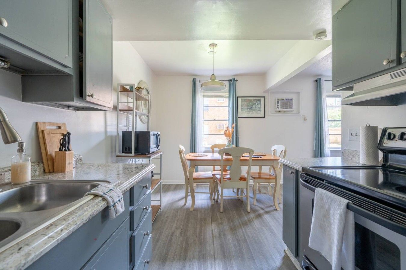A compact kitchen with a dining area, stainless steel appliances, and a window with curtains.