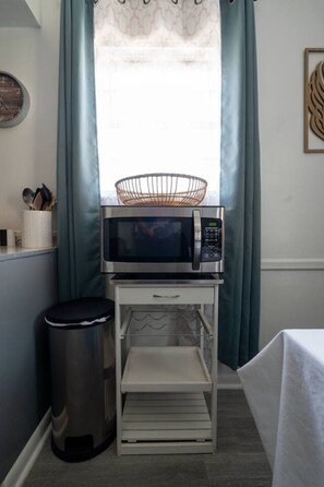Une petite cuisine équipée d’un four à micro-ondes, d’une petite poubelle et d’une étagère.