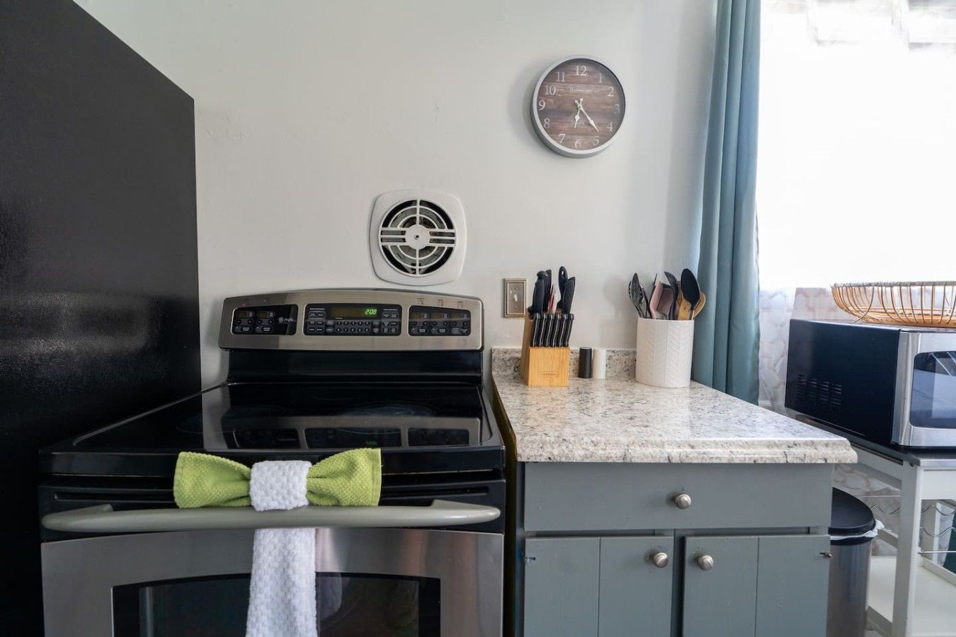 Una cocina con estufa, microondas y un reloj en la pared.