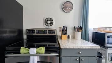 Een keuken met een fornuis, magnetron en een klok aan de muur.