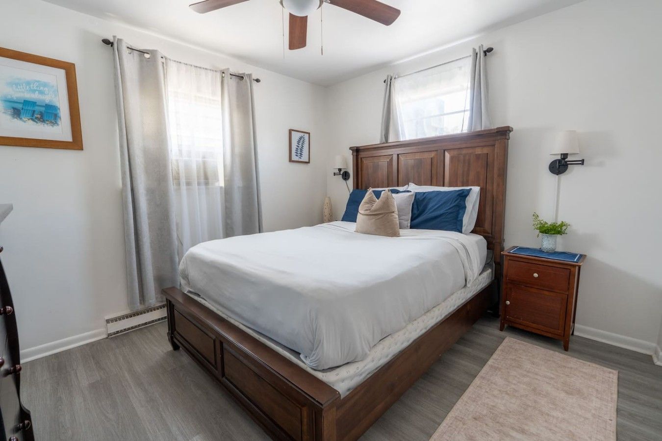 A bedroom with a wooden bed, a nightstand, a ceiling fan, and a window with curtains.