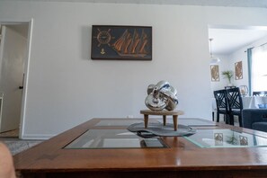 Un coin repas avec une table à plateau en verre, une sculpture en métal et une œuvre d’art encadrée accrochée au mur.