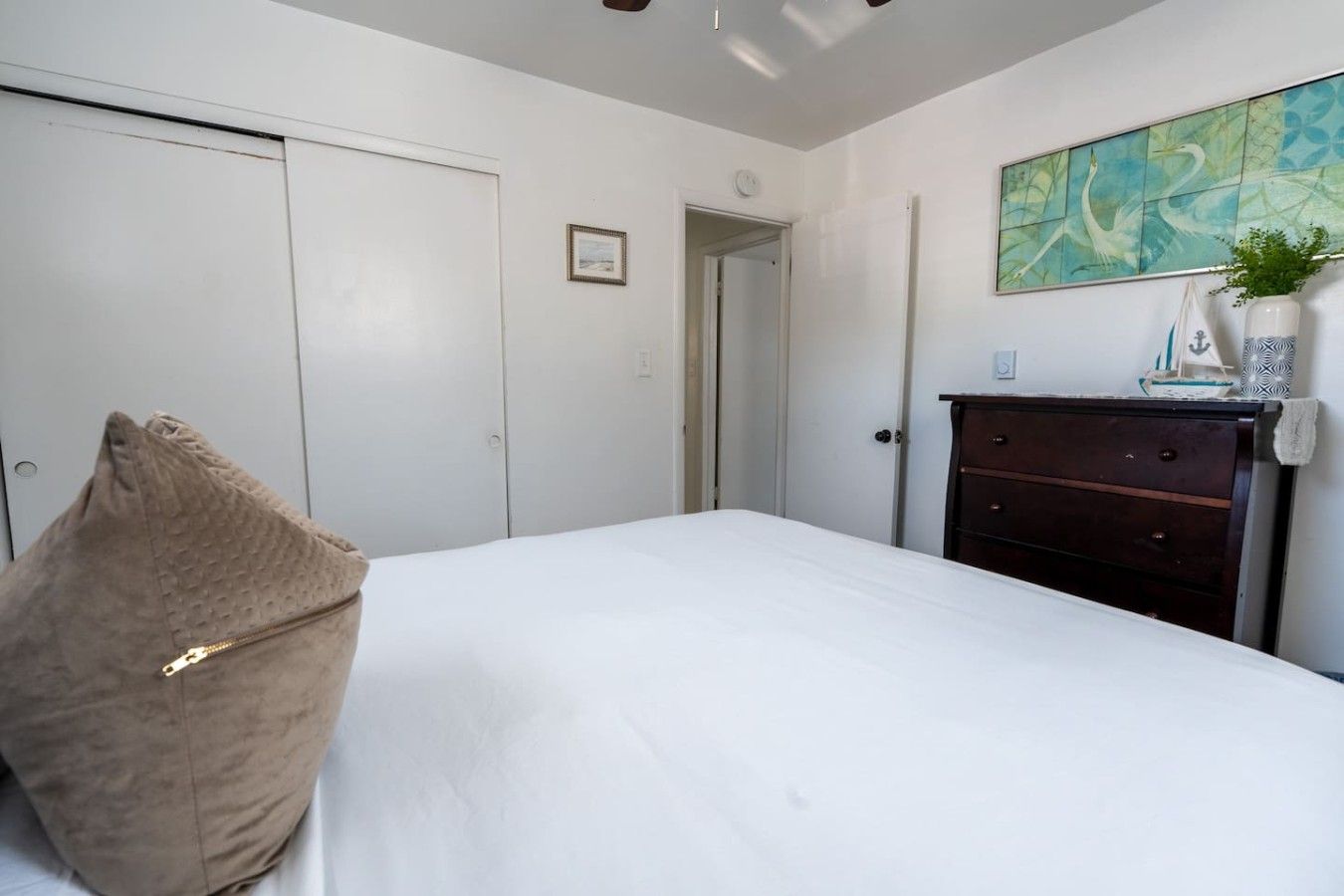 Een slaapkamer met een bed, een ladekast, een deur en een schilderij aan de muur.