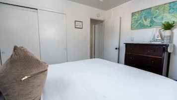 Een slaapkamer met een bed, een ladekast, een deur en een schilderij aan de muur.