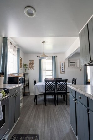 A compact kitchen with a dining area, featuring a central island, pendant lighting, and a view of the outdoors. - 2BR by Atlantic Park • Budget-Friendly Stay (Virginia Beach)