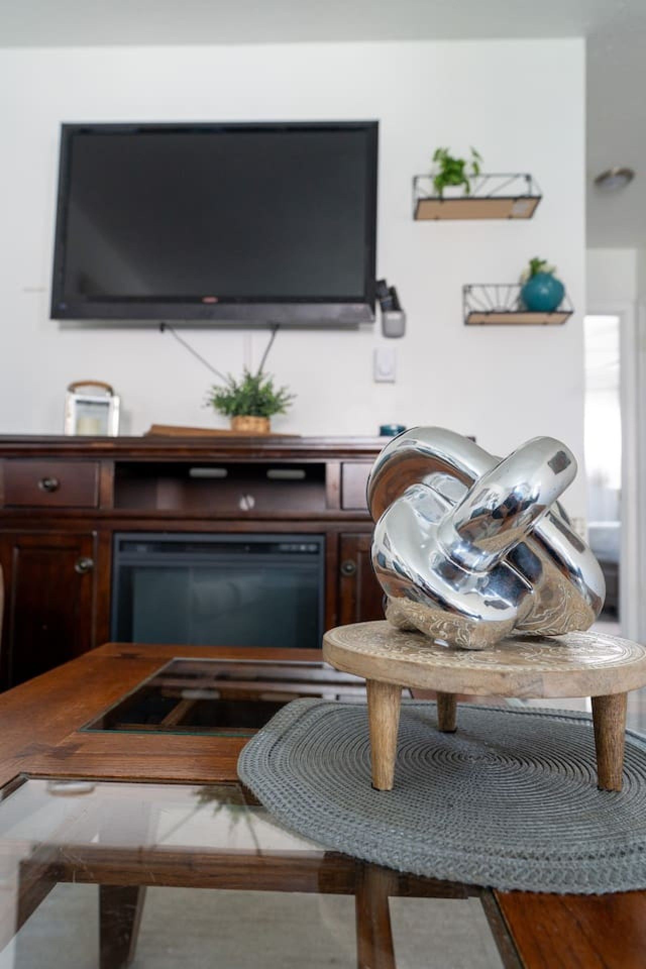 Una cocina moderna con televisión de pantalla plana montada en la pared, armarios de madera, horno empotrado y una mesa de comedor redonda con cubierta de vidrio.