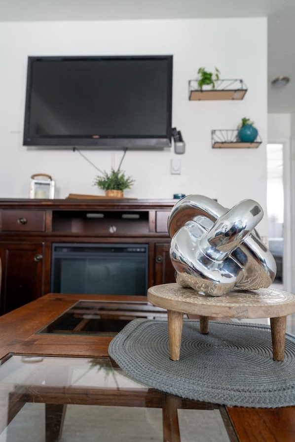 Een moderne keuken met een flatscreen televisie aan de muur, houten kasten, een inbouwoven en een ronde eettafel met een glazen blad.