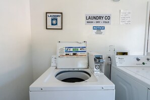 Een wasserette met een voorlader wasmachine, een wandgedroogde droger en een prikbord met wasinstructies.