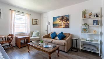 Een woonkamer met een bank, salontafel en een schilderij van een zonsondergang.