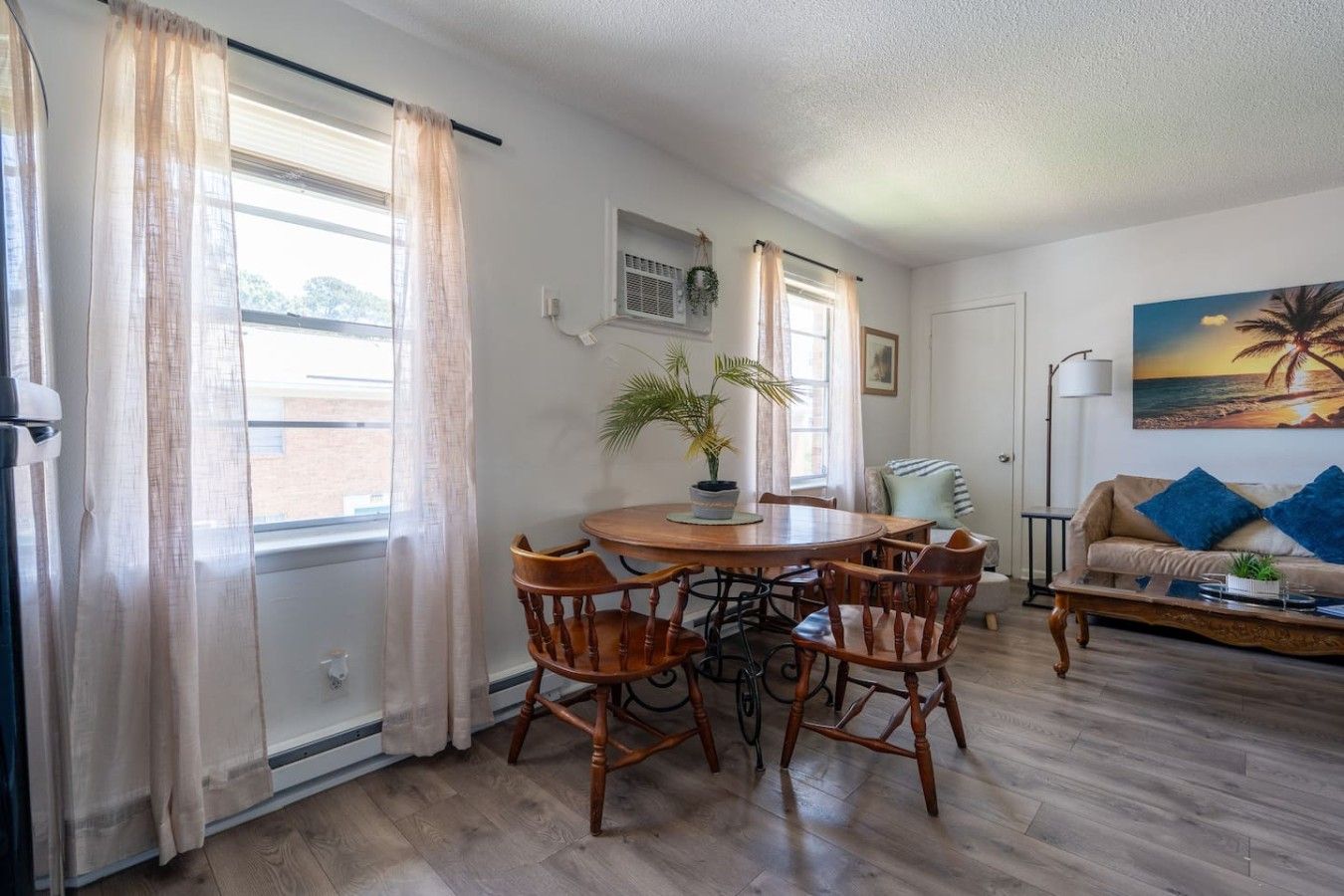 A room with a dining table, chairs, a sofa, and a painting on the wall.