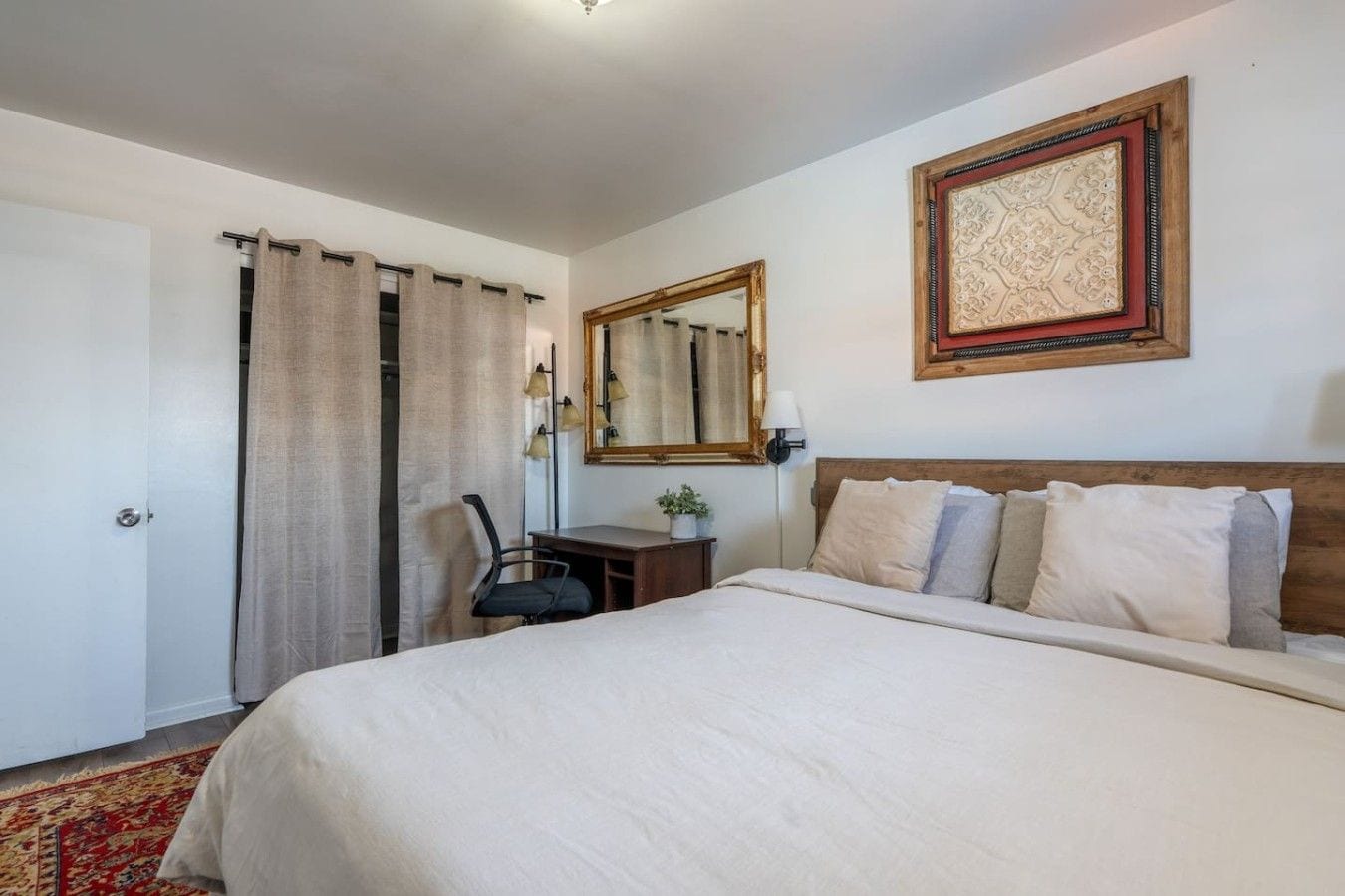 A hotel room with a bed, a desk, a chair, a mirror, and a door.