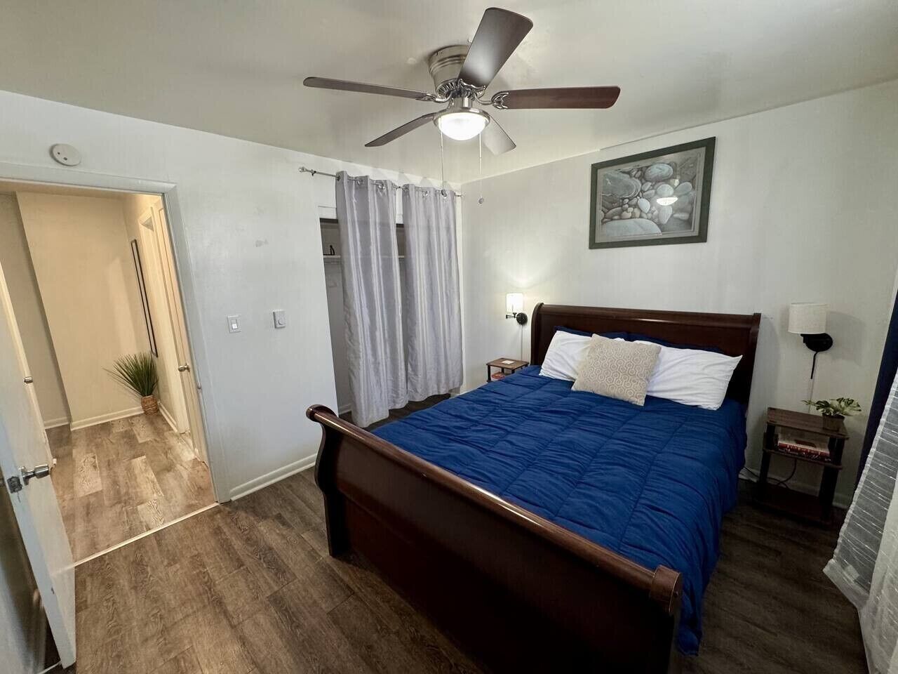 Une chambre à coucher avec un lit en bois, un ventilateur de plafond, une table de chevet avec une lampe et un tableau encadré au mur.