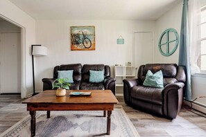 Un salón con dos sillones de cuero, una mesa de centro de madera, una lámpara de pie y un cuadro en la pared.