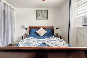 A bedroom with a wooden bed, a framed artwork on the wall, a bedside table with a lamp, and a window with curtains. - Mystique Blue 2 BR and Bath APT near Beach (Virginia Beach)