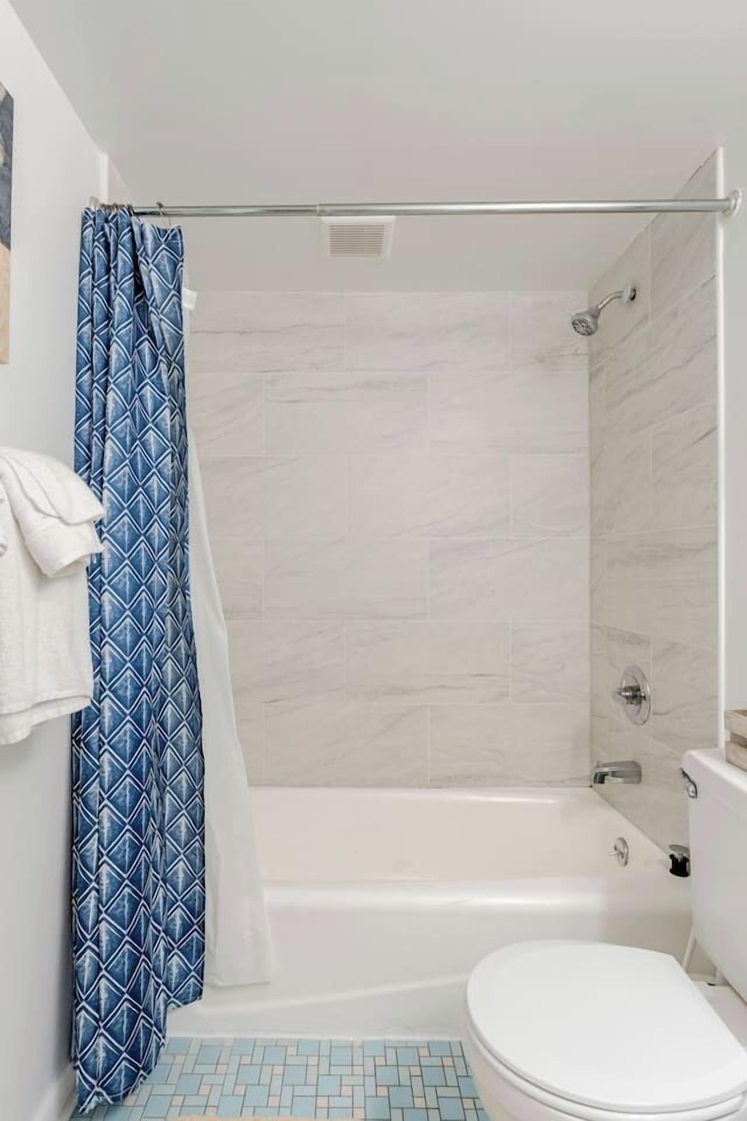 A bathroom with a shower, toilet, and a tiled floor.