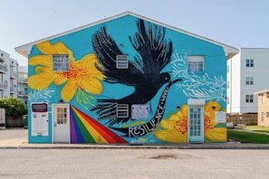 A building with a mural of a bird and flowers, a door, and a sign indicating short-term rental availability. - Oceanfront 2BR • Walk to Atlantic Park (Virginia Beach)