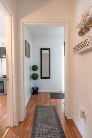 A hallway with a wooden floor, a black-framed mirror, and two spherical green plants. - Quiet 2BR • Walk to Beach, ViBe & The Dome (Virginia Beach)