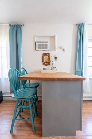 A kitchen with a wooden island, teal chairs, a white wall, and a window with curtains. - Quiet 2BR • Walk to Beach, ViBe & The Dome (Virginia Beach)