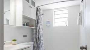 Ein Badezimmer mit Toilette, einer Badewanne, einem Duschvorhang, einem Fenster und einem Waschbecken mit Spiegel.