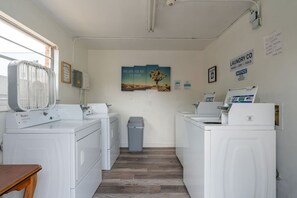 A laundry facility with two washers and dryers, a trash bin, and a poster on the wall. - Quiet 2BR • Walk to Beach, ViBe & The Dome (Virginia Beach)