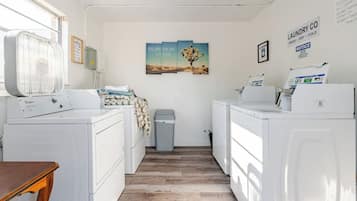 Een wasserette met een wasmachine, droger en een prullenbak. Er hangt een schilderij aan de muur en een bericht over de wasservices.