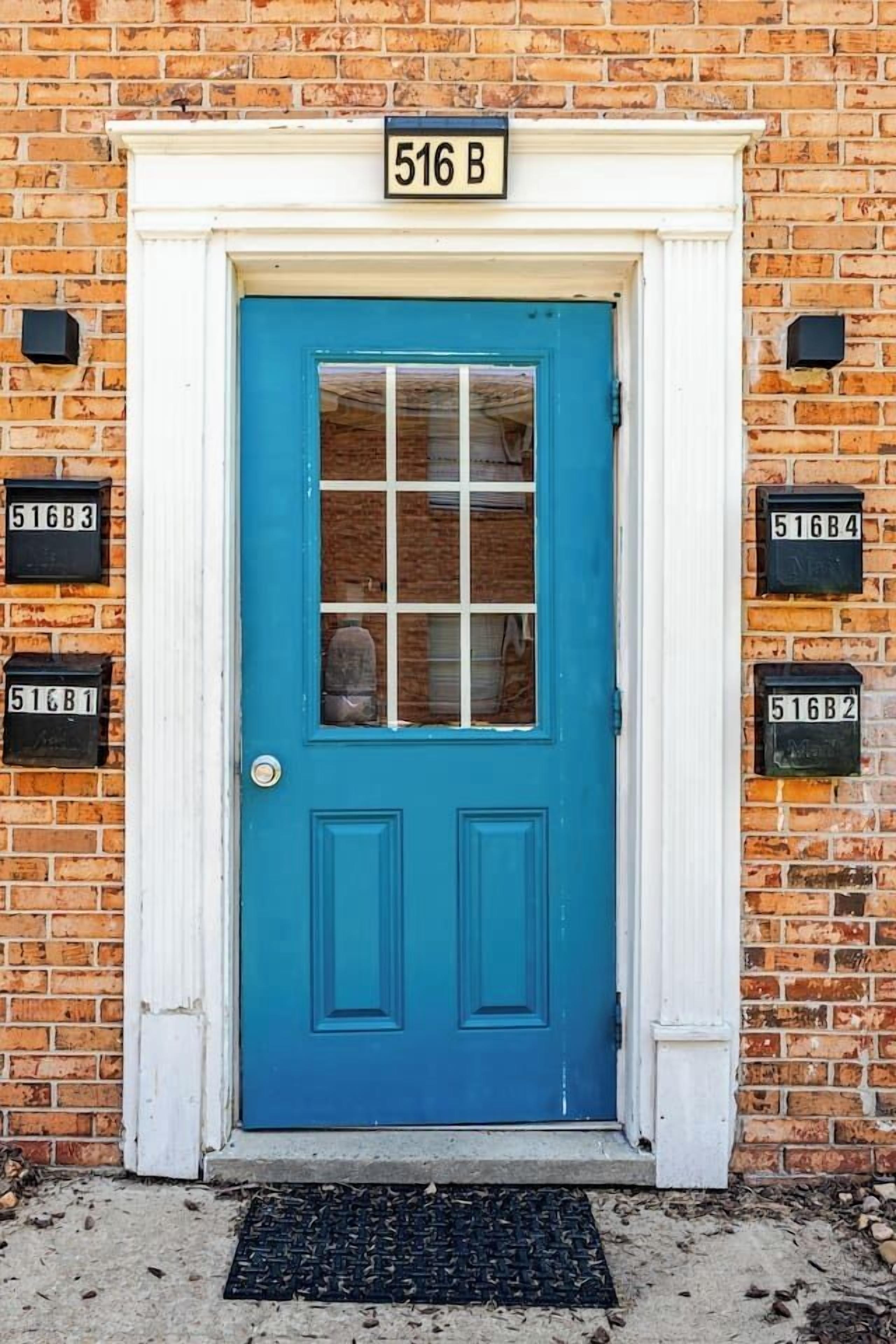 Une porte bleue avec un cadre blanc, une boîte aux lettres portant l’inscription « 516B », et un mur de briques.