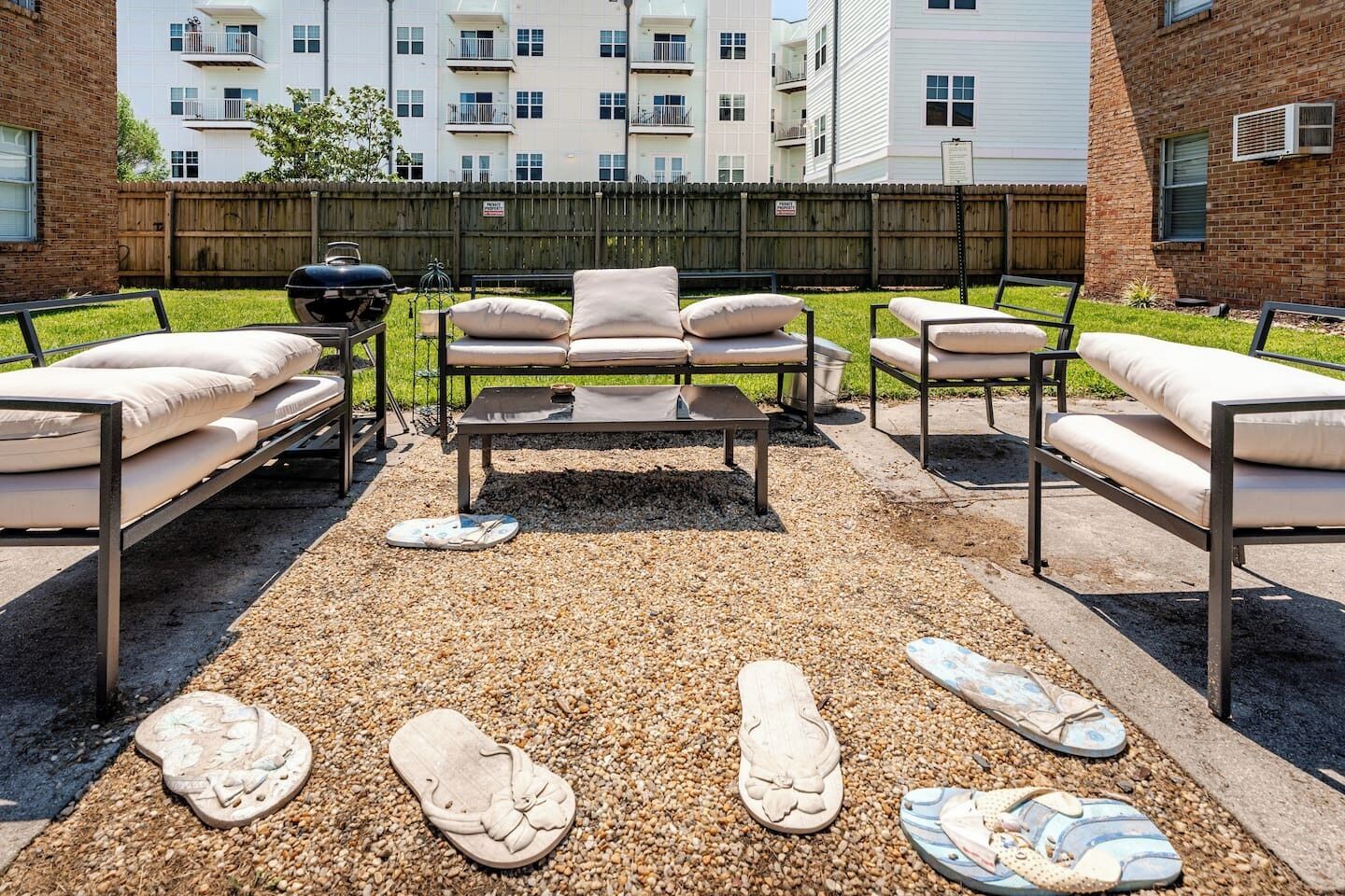 Un espace extérieur aménagé avec une table en métal et des canapés rembourrés, entouré de galets et de chaussures décoratives.