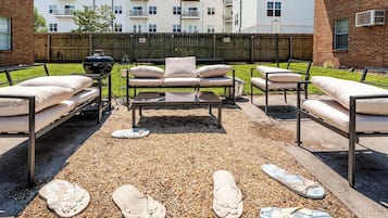 Un espace extérieur aménagé avec une table en métal et des canapés rembourrés, entouré de galets et de chaussures décoratives.