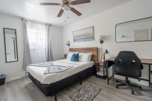 Habitación de hotel con cama, escritorio, silla, ventilador de techo y obra de arte en la pared.