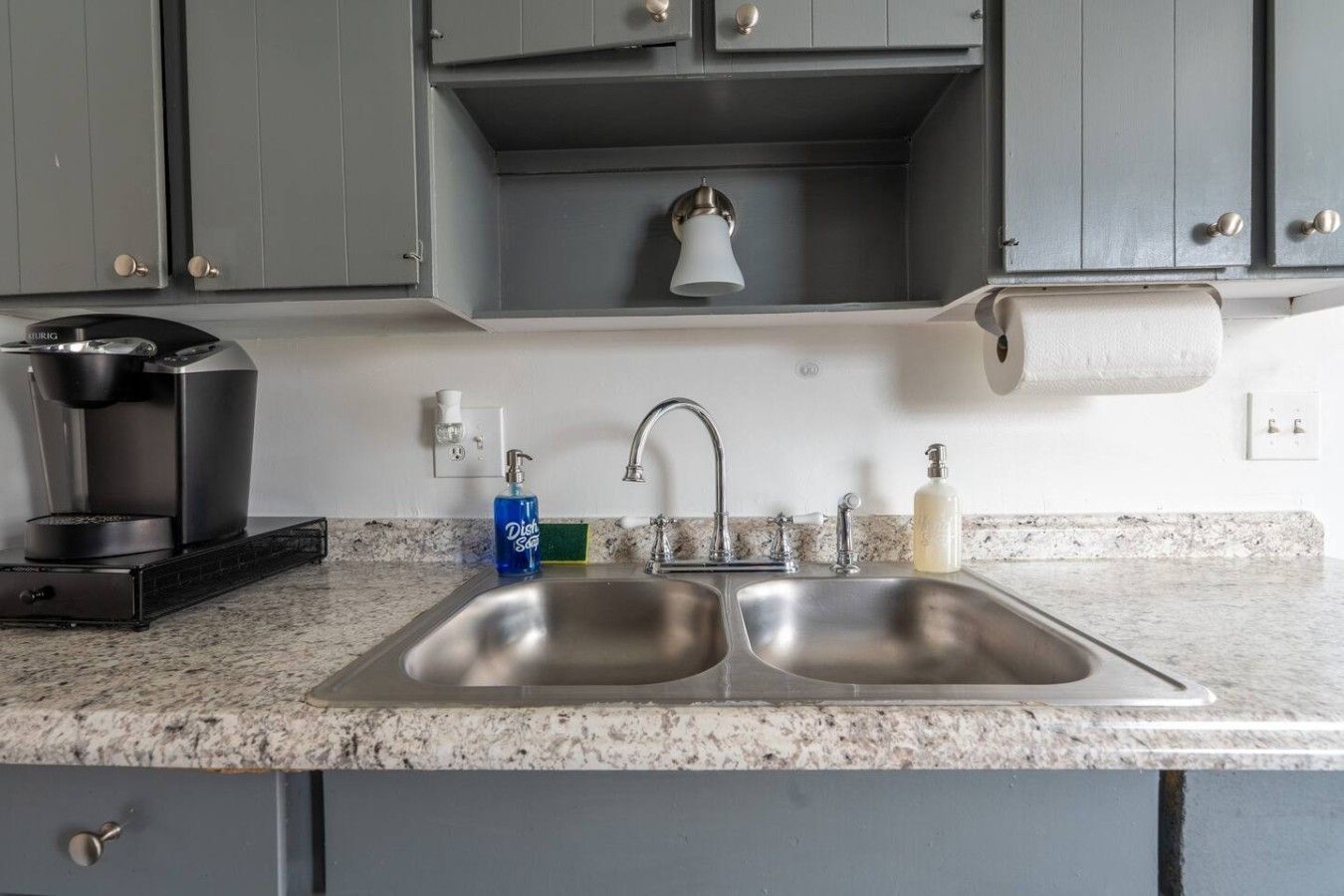 A kitchen with a double sink, a coffee maker, a soap dispenser, and a paper towel holder.
