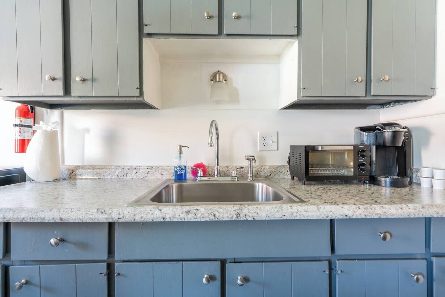 Een keuken met een granieten aanrecht, een roestvrijstalen spoelbak, een koffiezetapparaat, een magnetron en blauwe kastjes.