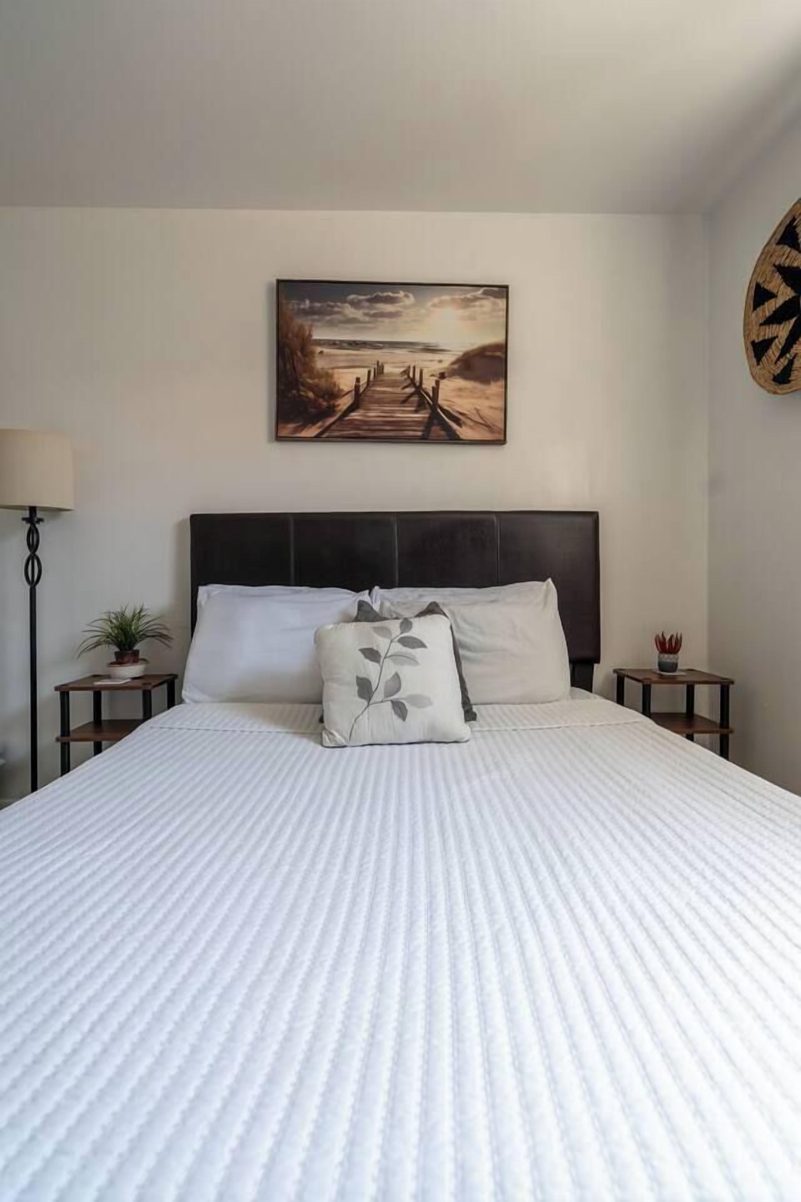 Een bed met hoofdbord, een nachtkastje met lamp en een kunstwerk aan de muur.