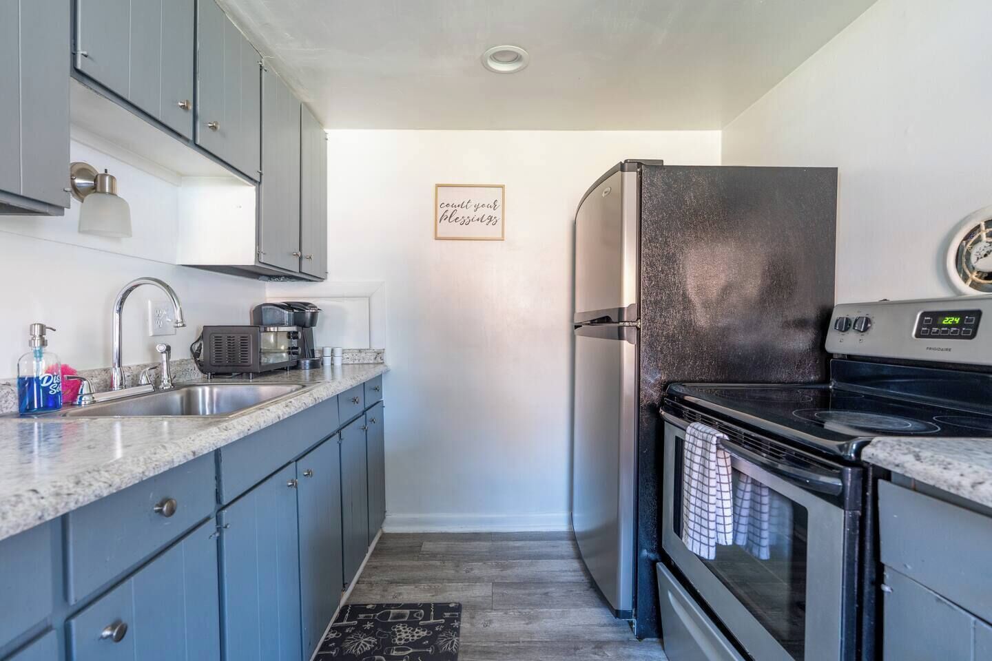 A compact kitchen with grey cabinets, a stainless steel refrigerator, a stove, and a coffee maker.