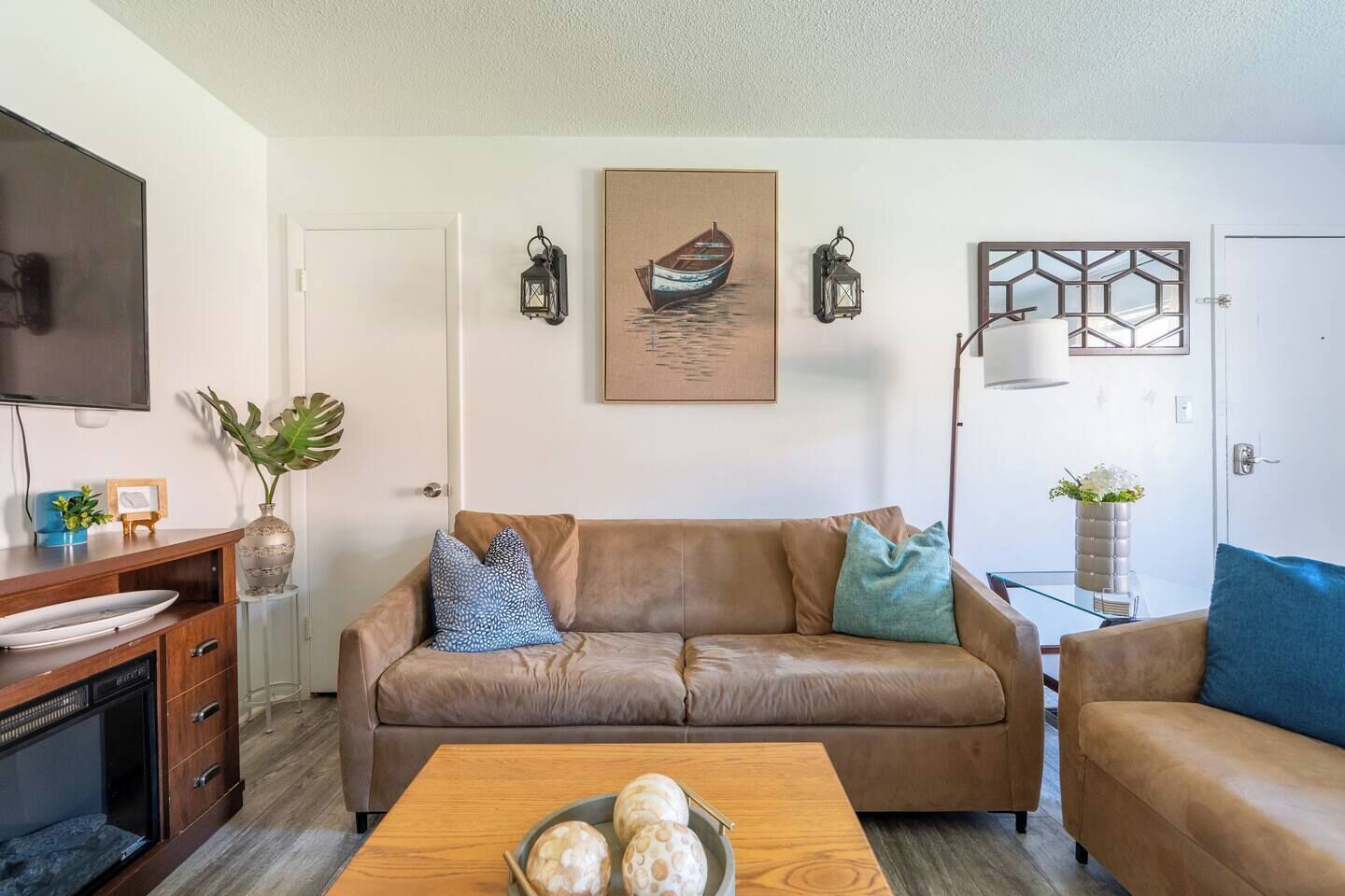 A living room with a brown leather sofa, a coffee table with decorative items, a flat-screen TV, and a framed picture of a boat on the wall.