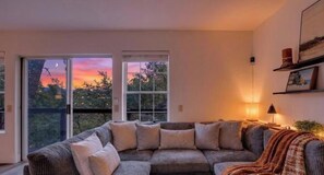 A living room with a sectional sofa, a lamp, and a view of the outdoors. - Cozy 3-bedroom cabin in amazing Copperopolis with AC and charm (Copperopolis)